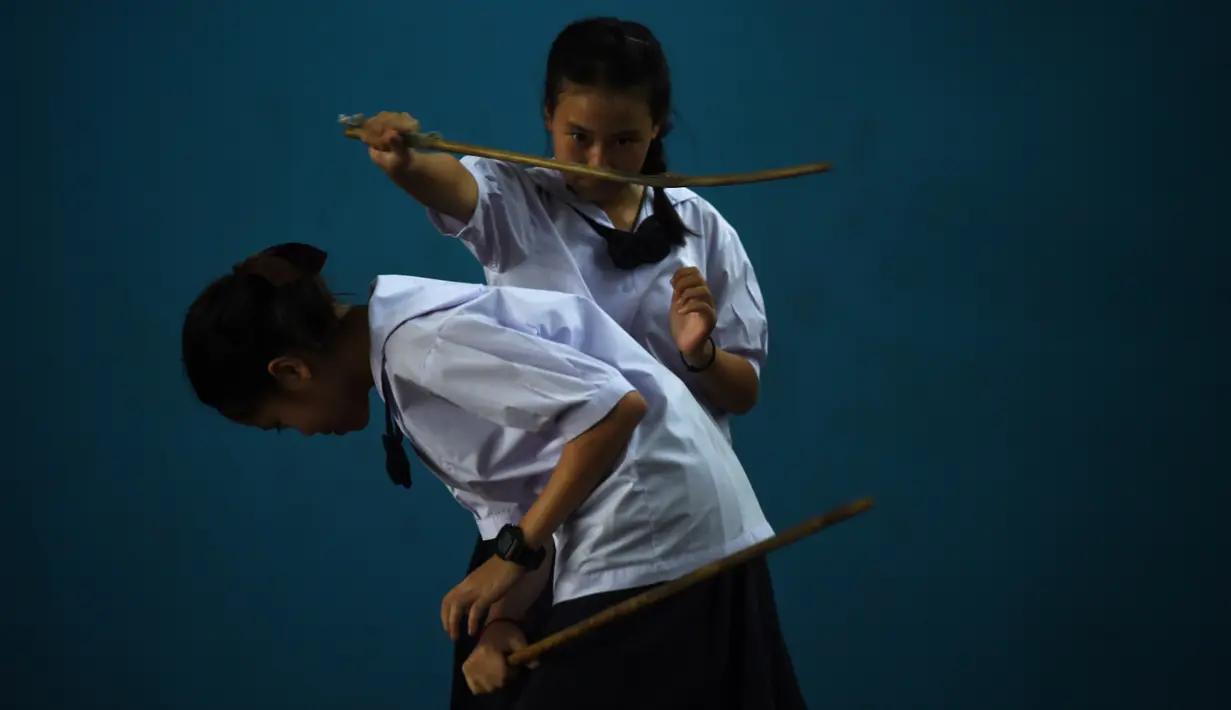 Dua siswi bertarung menggunakan pedang selama berlatih Krabi Krabong di sekolah Thonburee Woratapeepalarak, Thonburi, Bangkok (8/7/2019). Krabi Krabong merupakan seni bela diri Thailand yang dipersenjatai pisau dan perisai kayu. (AFP Photo/Lillian Suwanrumpha)