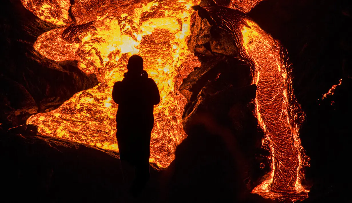 Seseorang menyaksikan aliran lahar dari letusan gunung berapi di Semenanjung Reykjanes, barat daya Islandia, Senin (29/3/2021). Letusan gunung berapi tersebut masih menarik ribuan orang yang berharap untuk mendekati aliran lahar. (AP Photo/Marco Di Marco)