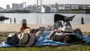 Orang-orang berbaring di rumput pada hari yang cerah di tepi teluk di daerah Odaiba Tokyo (12/4/2022). Odaiba yang dapat diakses dari Jembatan Pelangi atau kereta Yurikamome yang futuristik adalah pusat hiburan teknologi canggih di sebuah pulau buatan di Teluk Tokyo. (AFP/Charly Triballeau)