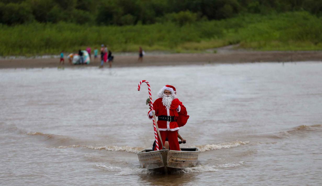 Relawan Jorge Alberto Barrozo, yang mengenakan kostum Sinterklas, berlayar dengan kano mengantarkan hadiah kepada anak-anak di komunitas tepi sungai di daerah pedesaan Careiro da Varzea, negara bagian Amazonas, Brasil pada Sabtu 20 Desember 2025. (Michael DANTAS/AFP)