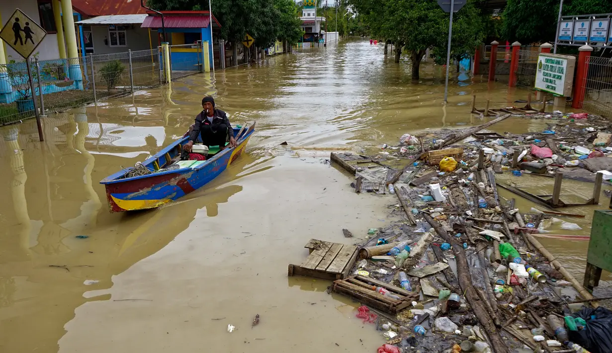 Seorang warga menggunakan perahu untuk melewati jalan yang tergenang banjir setelah hujan lebat dan tanggul jebol, di Lhoksukon, Aceh Utara, 7 Oktober 2022. (AFP/Azwar Ipank)
