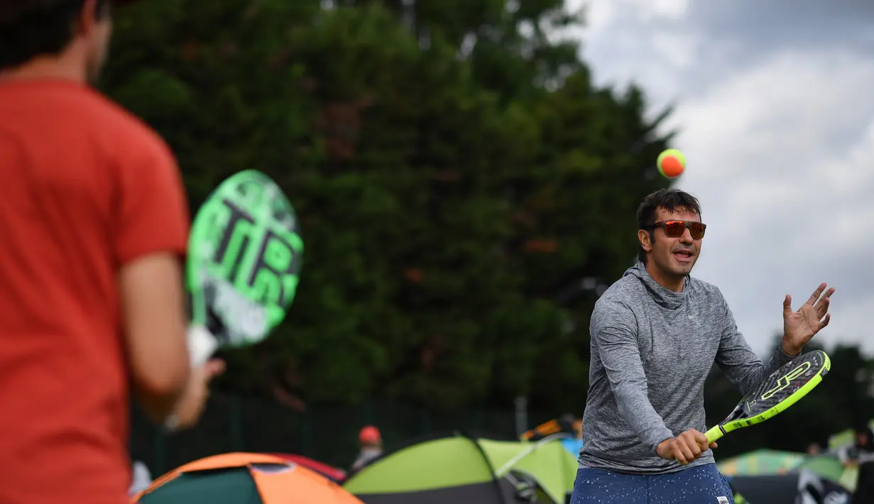 Dua pria bermain bola tenis ketika mereka mengantre untuk membeli tiket pada hari pertama turnamen tenis Kejuaraan Wimbledon 2019 di The All England Tennis Club di Wimbledon, London barat daya (1/7/2019). Turnamen ini dimulai 1 Juli-14 Juli 2019. (AFP Photo/Ben Stansall)