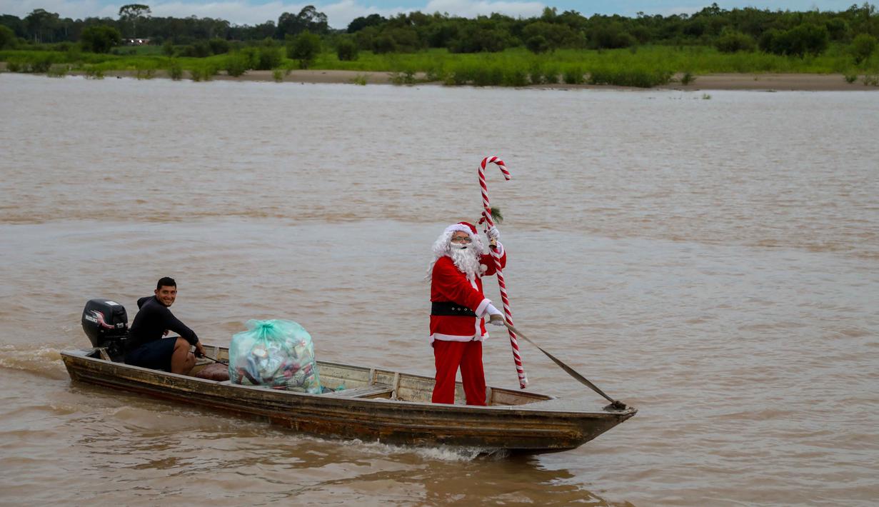 Pada Sabtu 20 Desember 2025, kelompok relawan Sahabat Sinterklas berbagi kebahagiaan Natal untuk untuk anak-anak di komunitas pedesaan dan tepi sungai di hutan hujan Amazon. Tampak dalam foto, relawan Jorge Alberto Barrozo, yang mengenakan kostum Sinterklas, berlayar dengan kano mengantarkan hadiah kepada anak-anak di komunitas tepi sungai di daerah pedesaan Careiro da Varzea, negara bagian Amazonas, Brasil pada Sabtu 20 Desember 2025. (Michael DANTAS/AFP)
