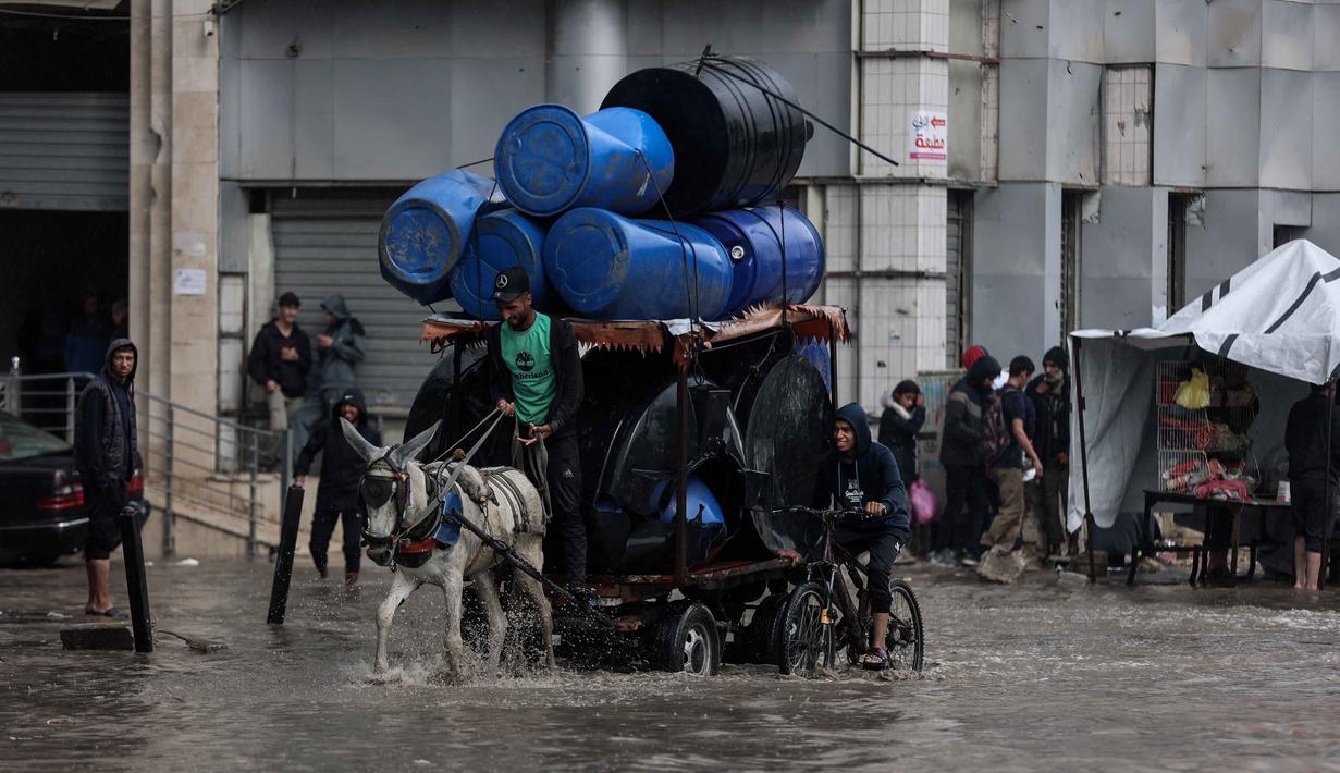 Sementara, ada lebih dari 170.000 orang terluka di Jalur Gaza sejak perang dimulai pada 7 Oktober 2023. Tampak dalam foto, seorang pria menunggang kereta kuda melewati banjir di kamp darurat yang menampung warga Palestina yang terlantar setelah hujan deras di Kota Gaza pada Selasa 25 November 2025. (Omar AL-QATTAA/AFP)