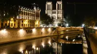 Pandangan umum dari Katedral Notre Dame tercermin di sungai Seine pada malam hari selama penerapan lockdown atau penguncian wilayah di Paris, 23 April 2020. Pandemi corona COVID-19 membuat Prancis menerapkan lockdown. (Ludovic MARIN / AFP)