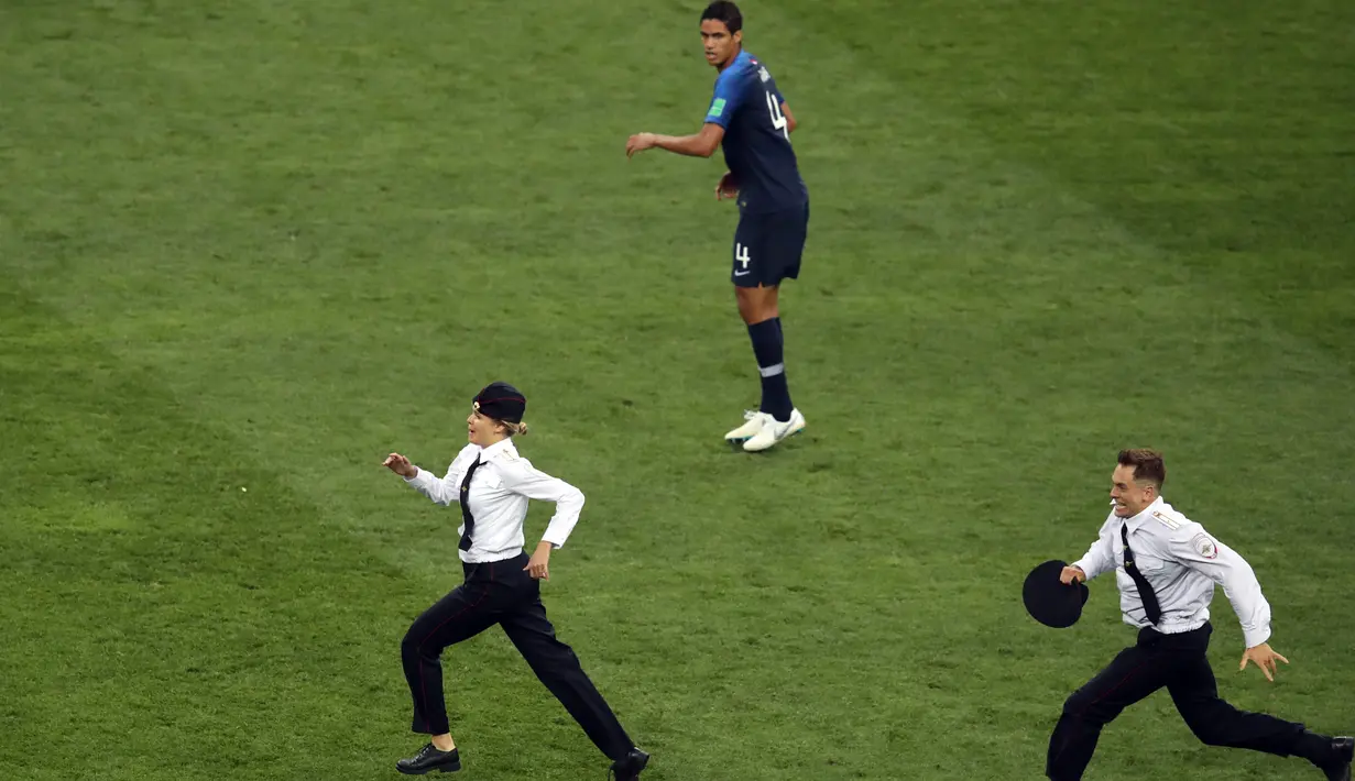 Pemain timnas Prancis, Raphael Varane melihat dua orang penyusup masuk ke lapangan pada laga final Piala Dunia 2018 melawan Kroasia di Luzhniki Stadium, Minggu (15/7). Empat orang berseragam polisi menyusup masuk ke dalam lapangan (AP/Thanassis Stavrakis)