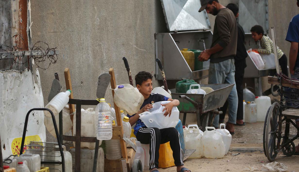 Warga Palestina yang mengungsi mengumpulkan air minum untuk dibawa kembali ke tempat penampungan mereka setelah rumah mereka hancur akibat bombardir Israel, di kamp pengungsi Bureij, Jalur Gaza Tengah pada Senin 18 Mei 2026. (Eyad Baba/AFP)