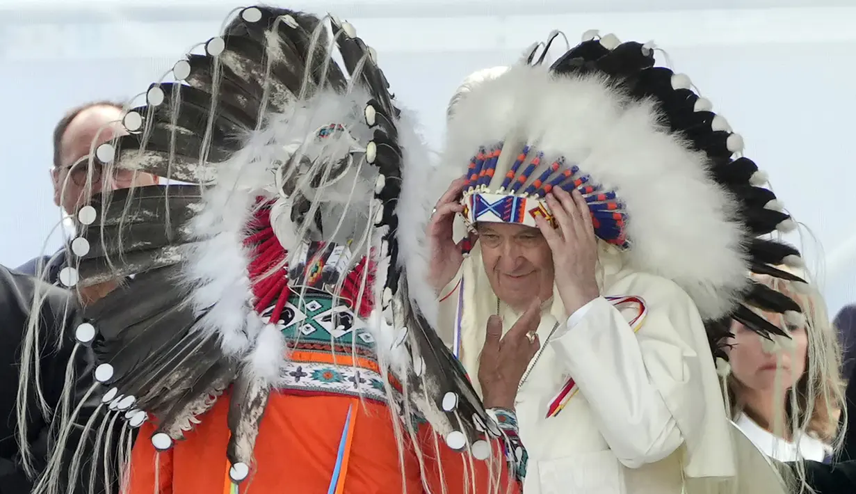 Paus Fransiskus mengenakan penutup kepala pribumi selama pertemuan dengan komunitas pribumi, termasuk First Nations, Metis, dan Inuit, di Gereja Katolik Our Lady of Seven Sorrows, Maskwacis, dekat Edmonton, Kanada, 25 Juli 2022. Berbicara kepada para korban di Maskwacis Senin sore, Paus Fransiskus mengungkapkan "kesedihannya", dan memohon para korban untuk mempraktikkan pengampunan, penyembuhan, dan rekonsiliasi terhadap Gereja Katolik atas peran yang dimainkannya dalam program sekolah bagi suku asli di Kanada. (AP Photo/Gregorio Borgia)