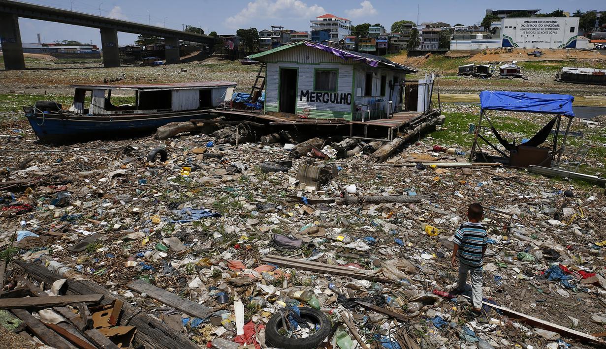 Anak laki-laki berjalan di samping rumah terapung yang terdampar di tempat yang dulunya merupakan tepi sungai Negro, di tengah kekeringan di Manaus, Brasil, Selasa, 26 September 2023. (AP Photo/Edmar Barros)