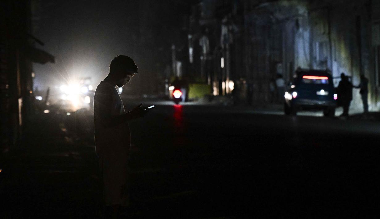 UNE juga mengumumkan bahwa upaya sedang dilakukan untuk memulihkan layanan listrik di seluruh negeri. Tampak dalam foto, seorang pria menggunakan teleponnya selama pemadaman listrik nasional di Havana, Kuba pada Sabtu 21 Maret 2026. (Yamil LAGE/AFP)