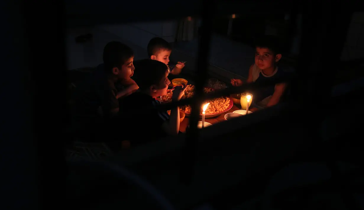 Sebuah keluarga Palestina menikmati makan sahur dengan penerangan lilin selama pemadaman listrik di kamp pengungsian Rafah, Jalur Gaza selatan, 11 Juni 2017. Selama ini Gaza menerima pasokan listrik Israel selama 3,5 jam setiap hari. (SAID KHATIB/AFP)