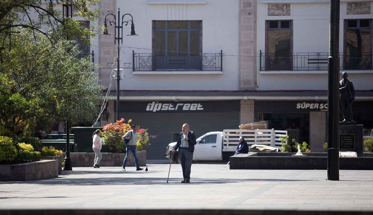 Tewasnya gembong narkoba ini memicu kerusuhan di berbagai negara bagian Meksiko. Tampak dalam foto, orang-orang berjalan di sepanjang jalan kosong yang dipenuhi toko-toko yang tutup di Morelia, negara bagian Michoacan, Meksiko, pada 23 Februari 2026. (Enrique Castro/AFP)