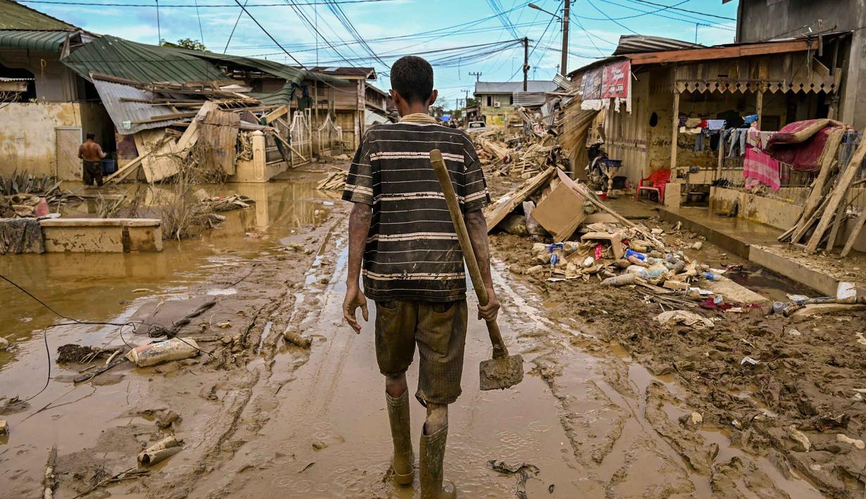 Seorang pria berjalan membawa cangkul di jalanan yang masih berlumpur setelah banjir bandang melanda daerah tersebut di Aceh Tamiang, Provinsi Aceh, pada Sabtu 6 Desember 2025. Gelombang penyakit ancam korban banjir Sumatra di Kabupaten Aceh Tamiang, Provinsi Aceh. (YT HARIONO/AFP)