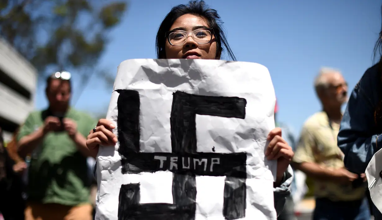 Seorang demonstran membawa poster bergambar Nazi saat demo menolak Donald Trump di Burlingame, California (29/4). Para wanita ini  menolak Donald Trump menjadi Presiden Amerika Serikat. (REUTERS/Noah Berger)