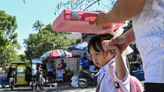 Seorang pria menggunakan tas sekolah untuk melindungi seorang anak dari sengatan matahari saat mereka meninggalkan sekolah di Manila, Filipina pada Senin 3 Maret 2025. (Jam STA ROSA/AFP)