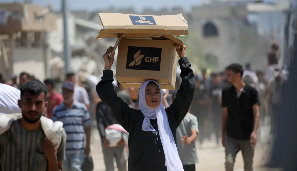 Seorang wanita Palestina membawa bantuan makanan ketika orang-orang kembali ke kamp pengungsi Nuseirat dari titik distribusi Yayasan Kemanusiaan Gaza yang didukung oleh Amerika Serikat (AS) di dekat koridor Netsarim, Jalur Gaza tengah, pada 27 Juli 2025. (Eyad BABA/AFP)