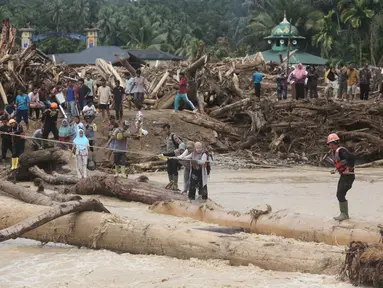 Warga yang menjadi korban banjir bandang di Batang Toru, Tapanuli Selatan, Sumatra Utara menggunakan kayu gelondongan untuk menyeberangi sungai, Selasa 2 Desember 2025. Warga Batang Toru, Tapanuli Selatan, terpaksa menggunakan jembatan darurat yang terbuat dari gelondongan kayu untuk menyeberangi sungai setelah jembatan utama rusak akibat terjangan banjir bandang baru-baru ini. (AP Photo/Binsar Bakkara)