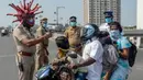 Inspektur polisi Rajesh Babu mengenakan helm berbentuk virus corona saat mengimbau pengendara motor selama lockdown di pos pemeriksaan di Chennai, India, Sabtu (28/3/2020). Cara ini bertujuan agar warga menerapkan social distancing dan tetap berada di rumah selama pandemi Covid-19. (Arun SANKAR/AFP)