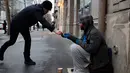 Seorang tunawisma menerima sejumlah uang saat dia duduk di jalanan di Paris, Senin (5/2). (AP Photo / Francois Mori)