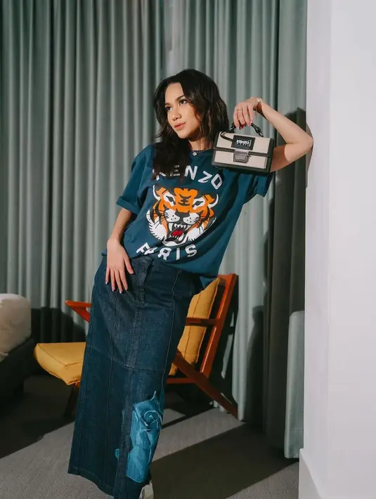 Azizah Salsha kembali tampil chic dengan kaus branded yang oversized, dipadunya mengenakan rok denim panjang bercorak bunga mawar pada bagian ujung bawahnya, dan tas tangan mini yang serasi. [Foto: Instagram/azizahsalsha_]