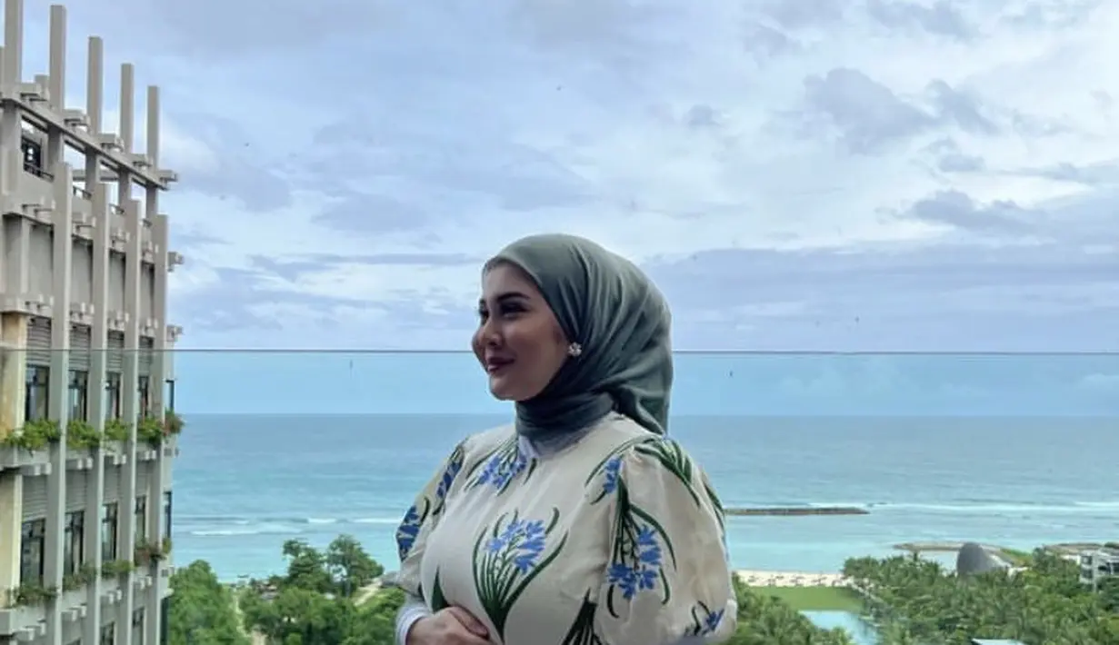 Ia juga tampil mengenakan maxi dress putih dengan motif flower dengan variasi lengan pump. Ia memadukannya dengan manset putih dan kerudung sagenya. (@kesharatuliu05)