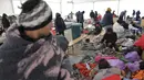 Para migran duduk di tempat penampungan sementara di kamp Lipa, barat daya Bosnia, dekat perbatasan dengan Kroasia, Sabtu (26/12/2020). Para imigran membungkus tubuh mereka dalam balutan selimut dan kantong tidur untuk melindungi diri dari serangan angin dingin yang menusuk. (AP Photo/Kemal Softic)