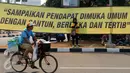 Seorang pedagang melintas di depan spanduk di pertigaan Medan Merdeka Selatan dan Barat saat ribuan buruh dari berbagai elemen organisasi melakukan aksi di depan Istana Negara, Jakarta, Selasa (1/9/2015). (Liputan6.com/Helmi Fithriansyah)