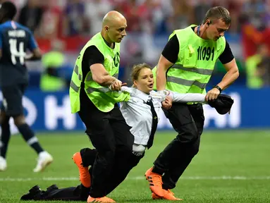 Petugas mengamankan seorang wanita yang menyusup masuk ke lapangan dalam laga final Piala Dunia 2018 antara Prancis dan Kroasia di Luzhniki Stadium, Minggu (15/7). Empat orang berlari masuk ke dalam lapangan menggangu jalannya laga. (AP/Martin Meissner)