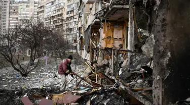 Seorang pria membersihkan puing-puing setelah peluru militer Rusia menghantam di sebuah bangunan tempat tinggal di Koshytsa Street, pinggiran ibukota Ukraina, Kiev (25/2/2022). Pasukan Rusia mencapai pinggiran Kyiv pada hari Jumat (24/2). (AFP/Daniel Leal)