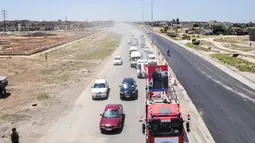 Kendaraan pemerintah dengan bendera nasional Suriah melintasi jalan raya utama antara Homs dan Hama yang dibuka kembali, Rabu (6/6). Pembukaan kembali jalan raya itu menandai kemenangan untuk Presiden Suriah Bashar al-Assad. (AFP/STRINGER)