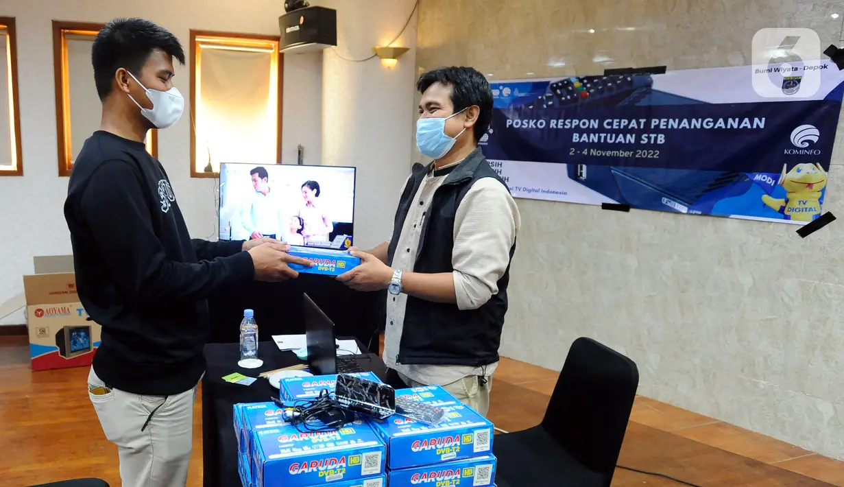 Petugas Kementerian Komunikasi dan Informatika (Kemenkominfo) memberikan alat Set Top Box (STB) yang dibagikan secara gratis kepada warga di Posko Respon Cepat Penanganan Bantuan STB di Hotel Bumi Wiyata, Depok, Jawa Barat, Rabu (2/11/2022). Kemenkominfo membuka posko penanganan bantuan STB sebagai perangkat konverter siaran TV digital ke televisi jenis analog bagi warga Jabodetabek yang akan mengikuti Analog Switch Off (ASO) di 2 November 2022 tengah malam. (merdeka.com/Arie Basuki)