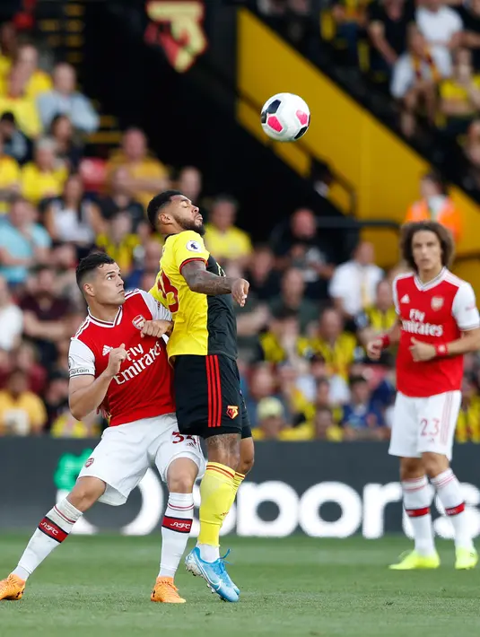 Andre Gray dari Watford berebut bola dengan kapten Arsenal, Granit Xhaka pada pekan kelima Liga Inggris 2019-2020 di Vicarage Road, Minggu (15/9/2019). Sempat unggul dua gol, Arsenal harus rela imbang 2-2 saat berjumpa tim tuan rumah Watford. (AP/Alastair Grant)