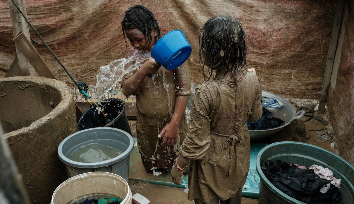 Berbagai gangguan kesehatan tersebut tidak terlepas dari kondisi lingkungan pasca-banjir yang masih tercemar. Tampak dalam foto, Baiti Arafah (kiri), 10 tahun, membersihkan diri dengan air sumur setelah bermain di genangan lumpur bersama adik perempuannya, Ria Mulyati Sara (7), di Babo, Aceh Tamiang, pada Senin 15 Desember 2025. (Yasuyoshi Chiba/AFP)