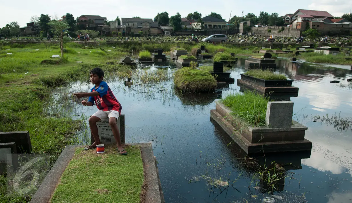 Seorang bocah bermain layang-layang diatas makam di Tempat Pemakaman Umum (TPU) Tanah Kusir, Jakarta, Selasa (25/4). (Liputan6.com/Gempur M. Surya)