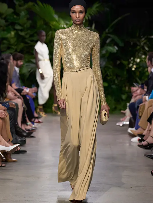 Baju lengan panjang model turtleneck keemasan yang dipadukan celana cokelat senada dengan pakaian dan clutchnya. Michael Kors