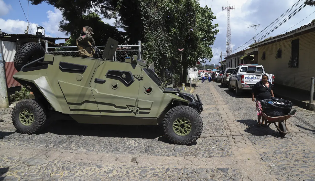 Seorang perempuan berjalan di depan mobil lapis baja tentara saat tentara berpatroli di jalan-jalan di Comasagua, El Salvador, Senin (3/10/2022). Geng-geng El Salvador, yang diperkirakan berjumlah sekitar 70.000 anggota, telah lama menguasai petak-petak wilayah dan memeras dan membunuh tanpa hukuman. (AP Photo/Salvador Melendez)