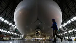 Petugas berjalan di depan The Airlander 10 saat peluncuran media di Cardington Airfield, Bedfordshire, Senin (21/3). Pesawat ini memiliki panjang  90 meter dan mempunyai lambung besar yang bisa dimasuki sebuah pesawat komersial. (ADRIAN DENNIS/AFP)