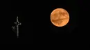 Momen langka ini hanya hadir setiap 18,6 tahun sekali. Tampak dalam foto, bulan purnama muncul di balik salah satu salib di Skopje, Makedonia pada 11 Juni 2025. (Robert ATANASOVSKI/AFP)