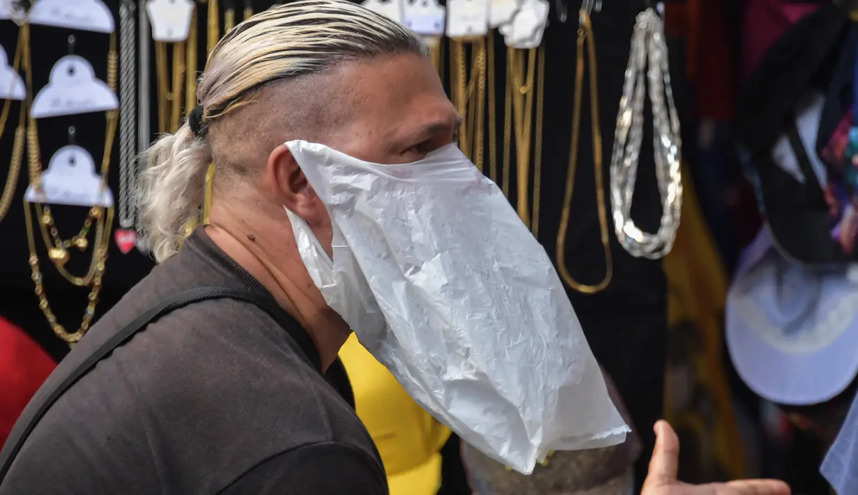 Seorang pedagang kaki lima memakai tas plastik sebagai masker di tengah pandemi virus corona baru, COVID-19, di pusat kota Sao Paulo, Brasil, pada 16 Maret 2020. Masker dijadikan masyarakat pilihan untuk mencegah penyebaran virus corona yang terus meningkat di seluruh dunia.  (NELSON ALMEIDA/AFP)