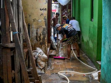 Warga membersihkan jalan di depan rumah mereka yang dipenuhi lumpur setelah banjir melanda lingkungan mereka setelah hujan deras di Jakarta pada Senin 7 Juli 2025. (BAY ISMOYO/AFP)
