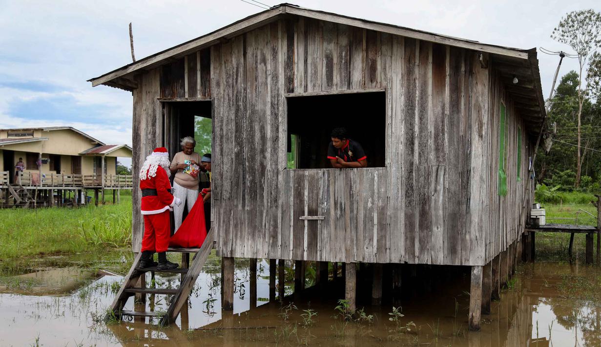 Berkostum ala Sinterklas, dengan menaiki sampan dan perahu, mereka datang untuk mengantar kado Natal untuk anak-anak. Tampak dalam foto, relawan Jorge Alberto Barrozo, yang mengenakan kostum Sinterklas, mengantarkan hadiah kepada warga di komunitas tepi sungai di daerah pedesaan Careiro da Varzea, negara bagian Amazonas, Brasil pada Sabtu 20 Desember 2025. (Michael DANTAS/AFP)