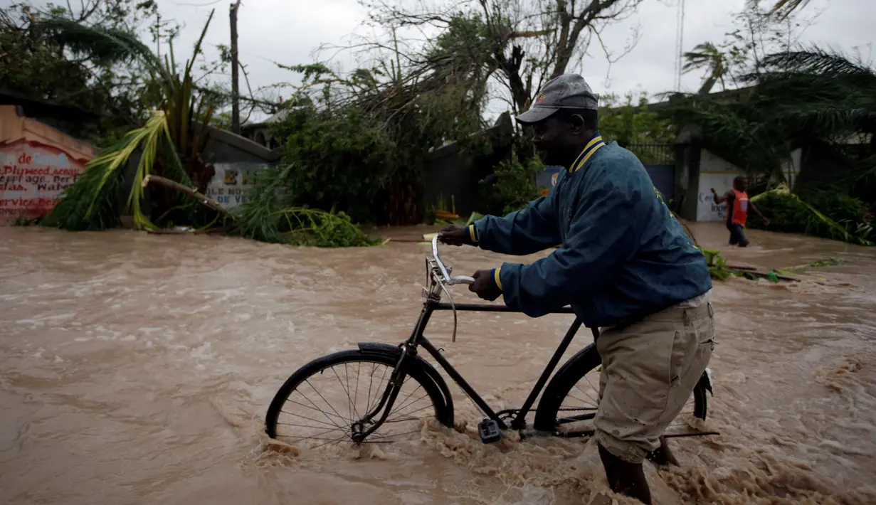 Seorang warga menuntun sepedanya saat melintasi banjir yang disebabkan oleh hantam Badai Matthew di Haiti (4/10). Keganasan Badai Matthew ini telah meluluhlantakkan wilayah Haiti. (REUTERS/Andres Martinez Casares)