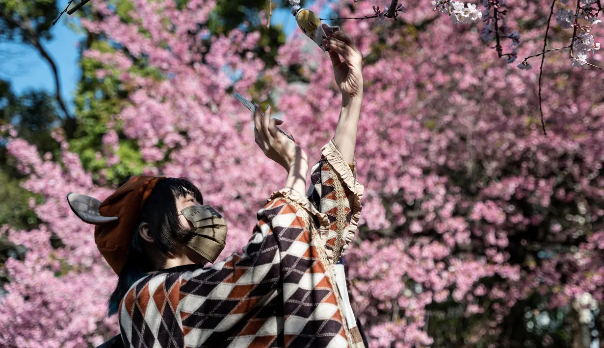 Seorang perempuan muda mengambil foto boneka saat orang-orang keluar ke Taman Ueno untuk melihat bunga sakura awal di Tokyo pada 14 Maret 2023. Pengunjung taman Ueno di Tokyo menikmati bunga sakura yang mekar lebih awal dari biasanya pada musim ini.  (Photo by Richard A. Brooks / AFP)