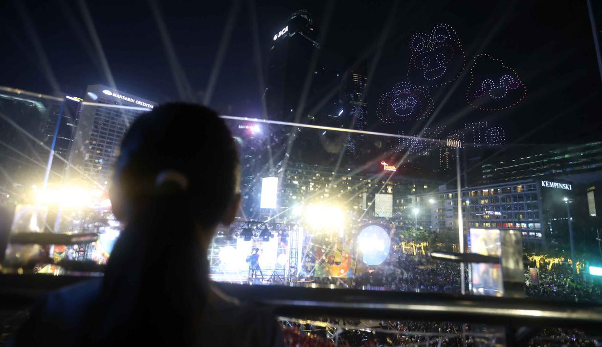 Formasi kemudian berubah-ubah, menampilkan berbagai tampilan visual lainnya di udara, seperti slogan “Road to Jakarta 500” serta maskot Je, Ka, dan Te. Tampak dalam foto, warga mengabadikan pertunjukan drone saat perayaan malam pergantian tahun di kawasan Bundaran Hotel Indonesia, Jakarta, Rabu (31/12/2025). (Kapanlagi.com/Budy Santoso)