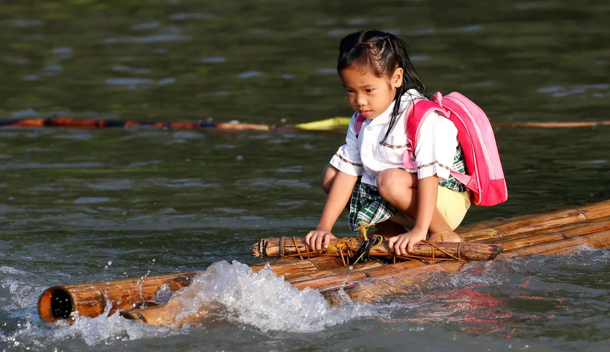 Seorang bocah memegang erat kayu di perahu rakit saat ingin menuju sekolah di sebuah desa terpencil di Montalban, Rizal, Filipina, Senin (13/6). Tidak adanya fasilitas jembatan membuat para siswa mempertaruhkan keselamatannya. (REUTERS/Erik De Castro)