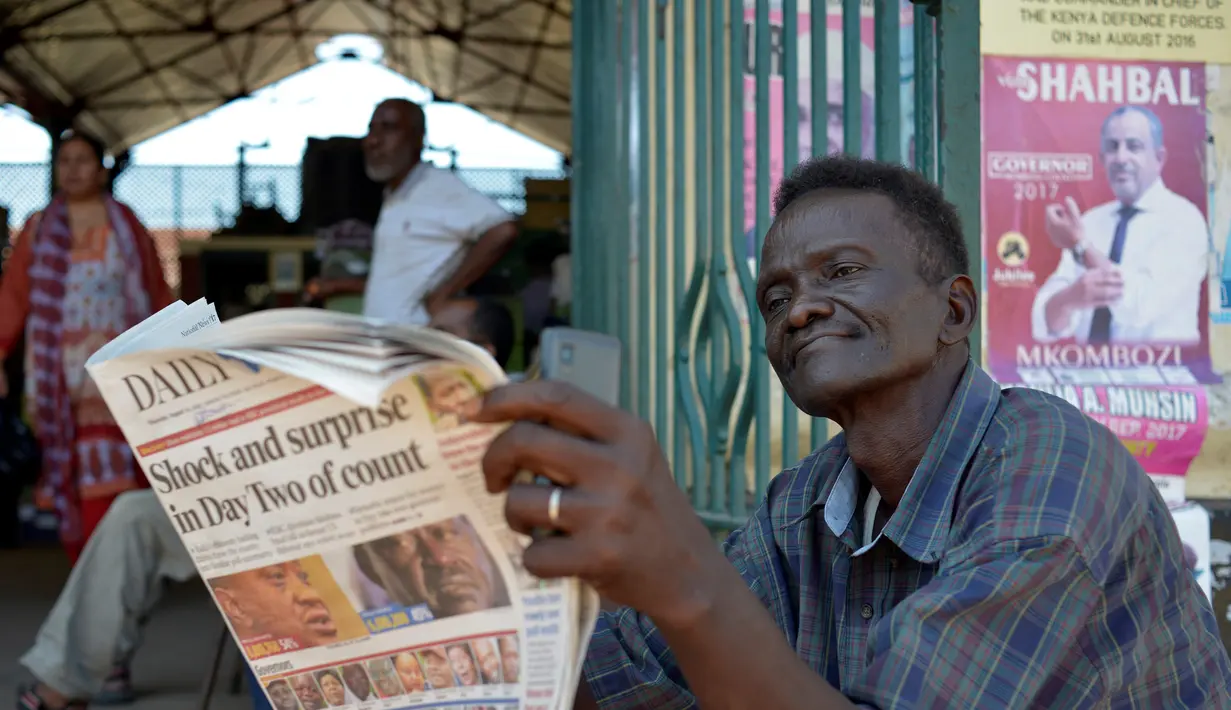 Seorang pria membaca koran sambil menunggu hasil resmi pemilihan umum Kenya di luar pasar sentral di Mombasa (10/8). Warga Kenya tengah menunggu hasil pemilihan presidennya, antara Uhuru Kenyatta dan pesaingnya, Raila Odinga. (AFP Photo/Tobin Jones)
