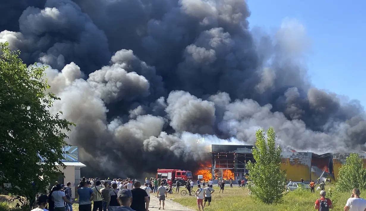 Orang-orang menyaksikan asap mengepul setelah serangan roket Rusia menghantam pusat perbelanjaan yang ramai, di Kremenchuk, Ukraina (27/6/2022). Pejabat Ukraina mengatakan sejumlah warga sipil dikhawatirkan tewas atau terluka setelah serangan rudal Rusia menghantam pusat perbelanjaan yang ramai di pusat kota Kremenchuk. (Viacheslav Priadko via AP)
