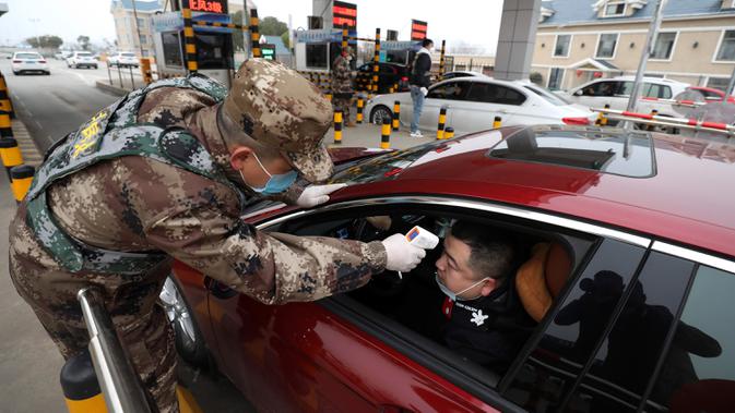 Anggota milisi mengukur suhu pengemudi mobil di sebuah pos pemeriksaan gerbang tol di Wuhan, Provinsi Hubei, China, Kamis (23/1/2020). Pemerintah China mengisolasi Kota Wuhan yang berpenduduk sekitar 11 juta jiwa untuk menahan penyebaran virus corona. (Chinatopix via AP)