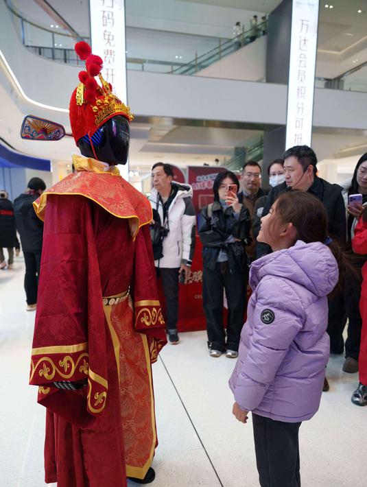 Pada pameran ini, pengunjung dapat menyaksikan berbagai jenis robot, termasuk humanoid dan yang berkaki empat (robot anjing), yang melakukan gerakan tarian untuk menyambut Tahun Baru Imlek 2577 Kongzili. Tampak dalam foto, seorang anak melihat robot humanoid yang berpakaian seperti Dewa Kekayaan selama pratinjau media pameran kuil robot yang dirayakan menjelang Tahun Baru Imlek di Beijing, China, Jumat 13 Februari 2026. (AP Photo/Vincent Thian)