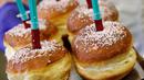 Pekerja berpose sambil membawa berliner (donat Jerman) dengan jarum suntik penuh raspberry jelly di toko roti Kreyenbuhl di Muri, Swiss pada 5 Februari 2021. Merespons hadirnya vaksin Covid-19, toko roti Kreyenbuhl mencoba merayakannya dengan membuat "Vaccine Berliners". (STEFAN WERMUTH/AFP)